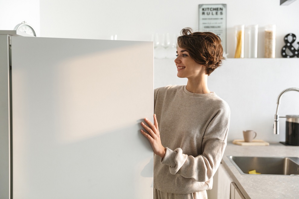 אישה צעירה מאושרת עומדת ליד המקרר שנפתח